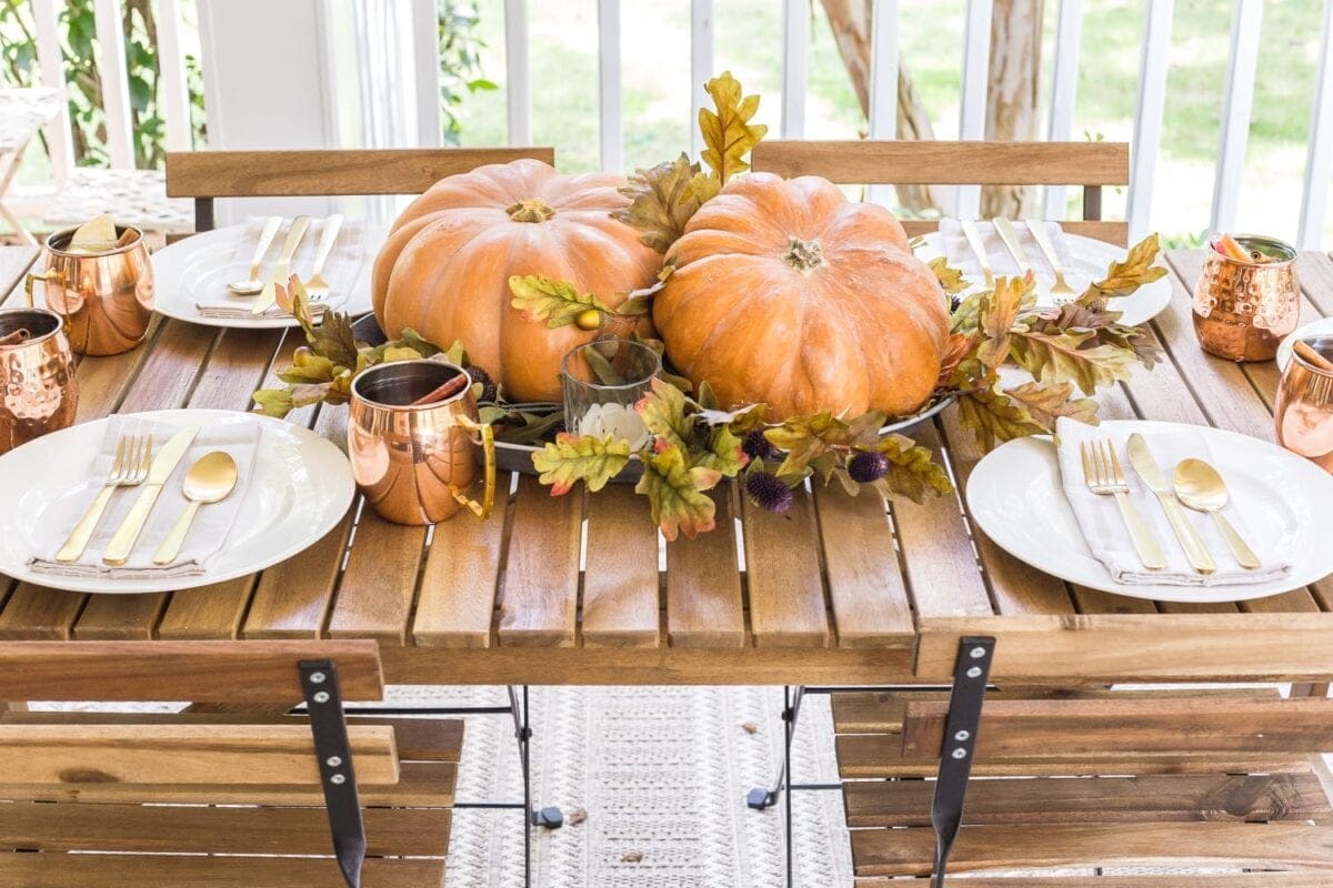 simple fall centerpiece made of a platter, leaves, and two pumpkins in the middle of an outdoor dining table