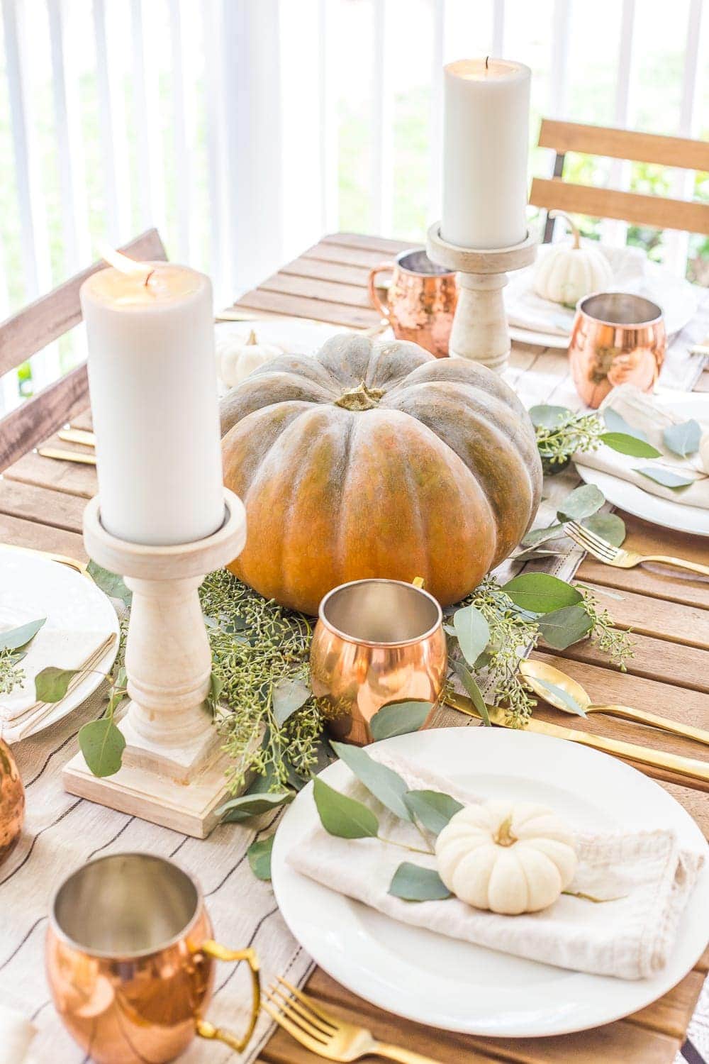 DIY fall centerpiece of simple pumpkin with eucalyptus leaves and pillar candles