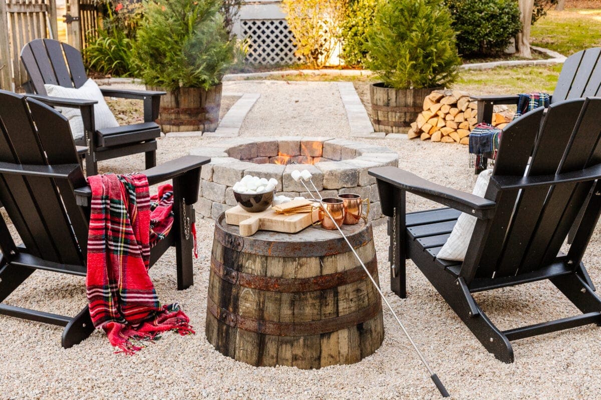 stone diy fire pit with pea gravel, stone edgers, and adirondack chairs with a barrel planter as a side table
