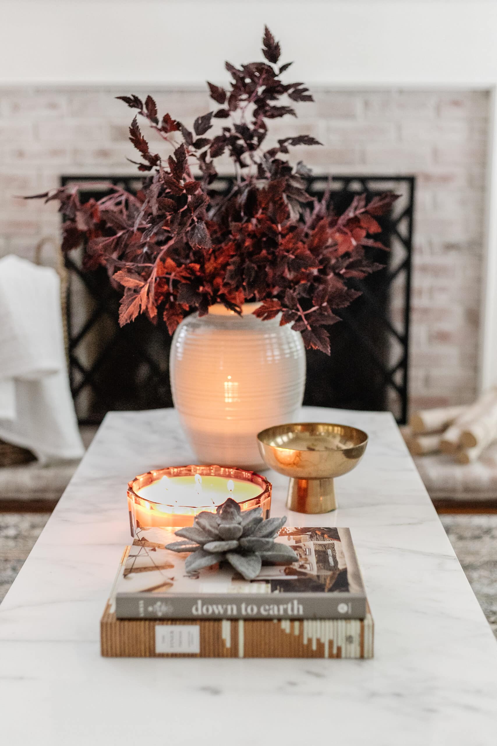 coffee table with vase of fall branches, candle, brass bowl, and stack of books