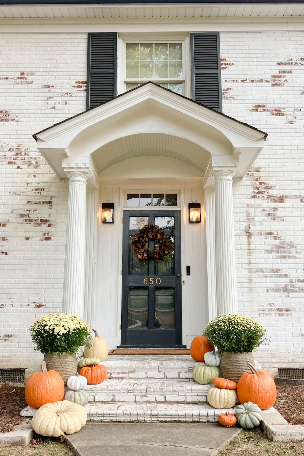front porch decorated for fall with fake pumpkins and mums on porch steps with limewashed brick
