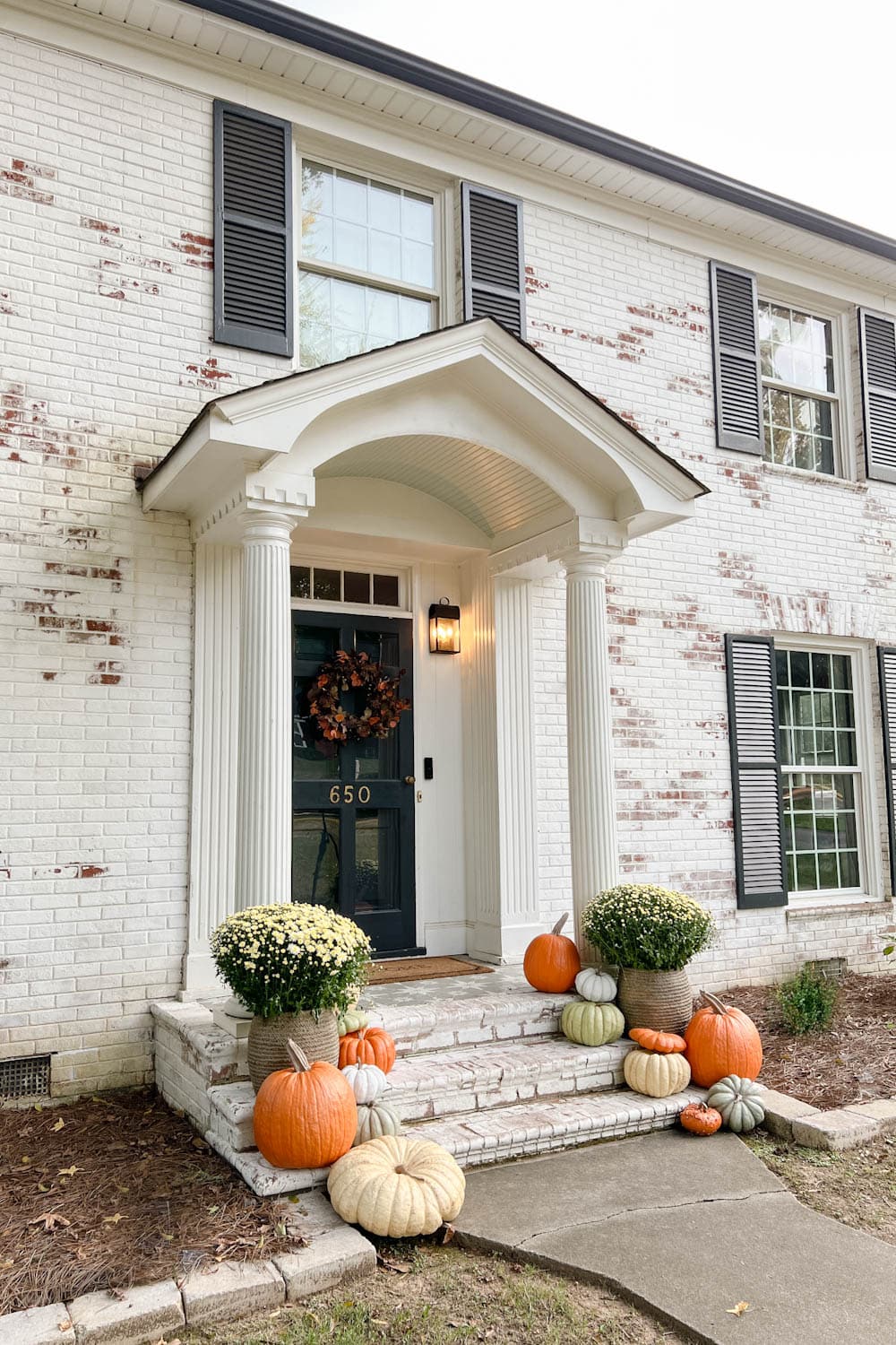 fall front porch on a limewashed brick colonial house with artificial pumpkins on steps