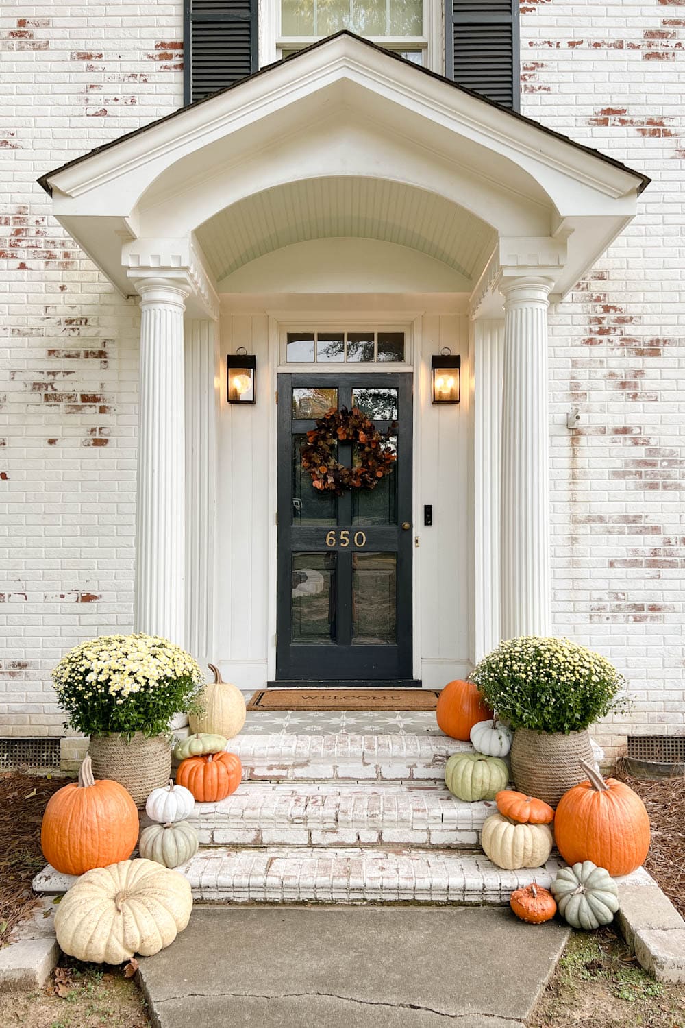 fall front porch with potted mums, wreath, and realistic fake pumpkins on steps
