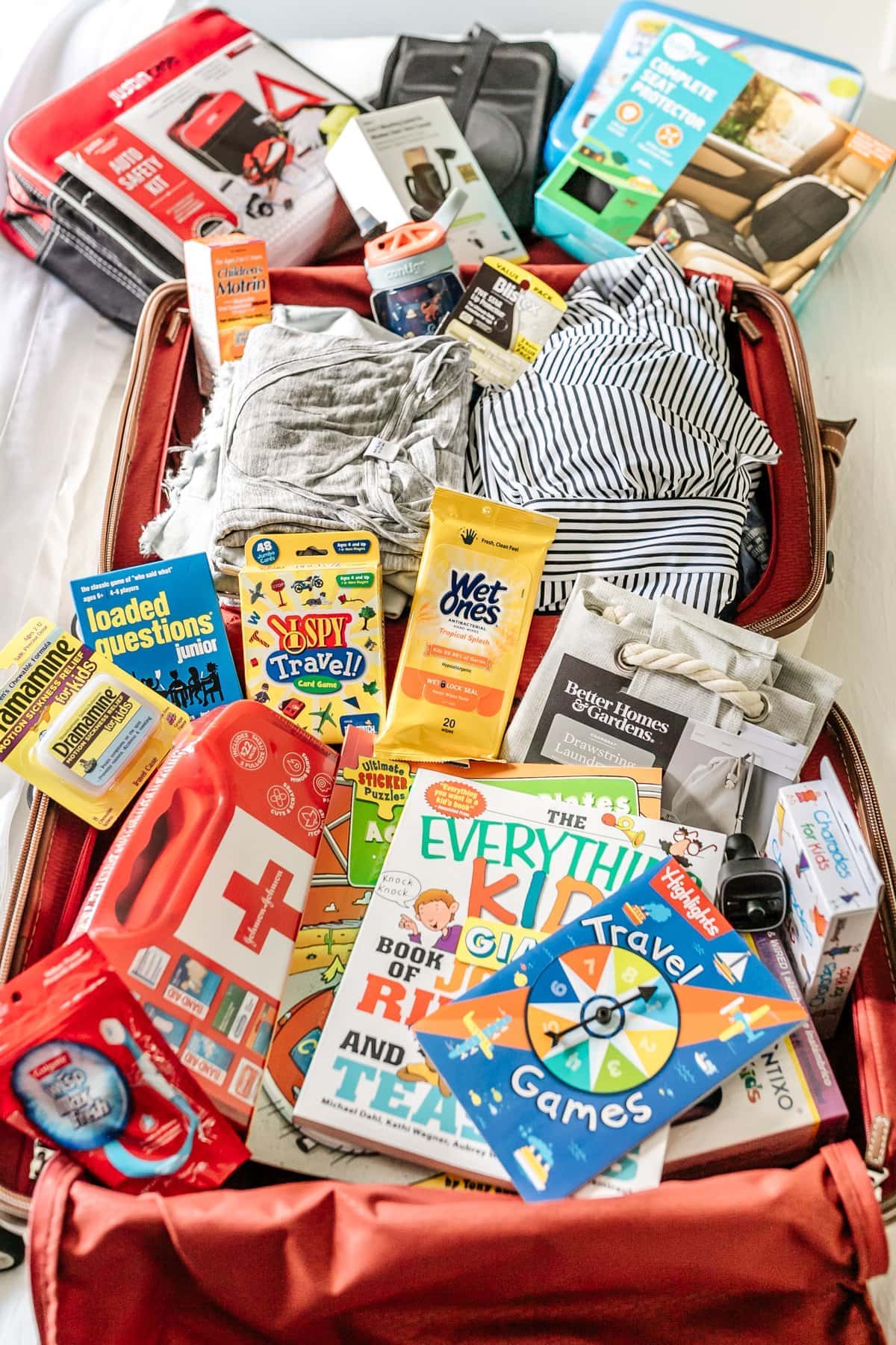 suitcase packed with travel essentials like travel games, first aid kit, wet wipes, Dramamine, and car organizers